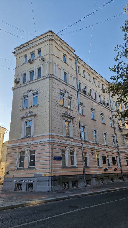 Фасад многоэтажного доходного дома на Спиридоновке: светлая штукатурка, симметричные окна и архитектурные детали эпохи модерна в городской улице.