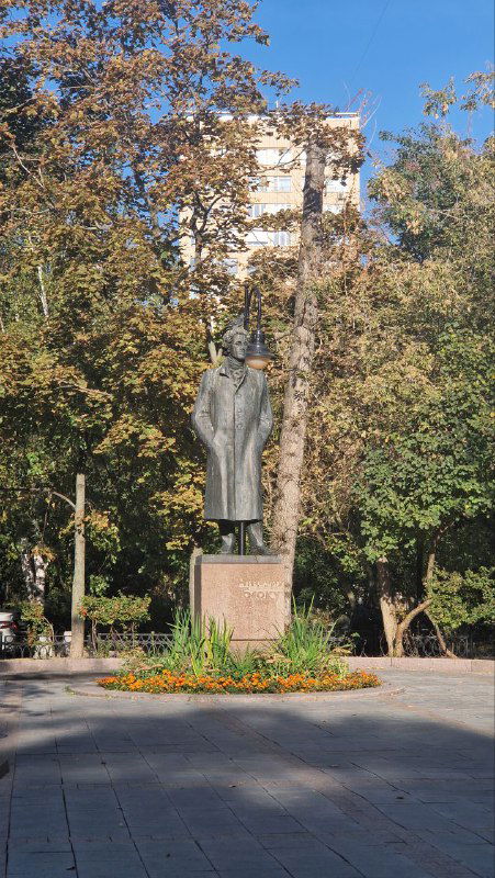 Памятник поэту в сквере на Спиридоновке: бронзовая скульптура на каменном постаменте, окружённая деревьями и ухоженной клумбой в городской аллее.