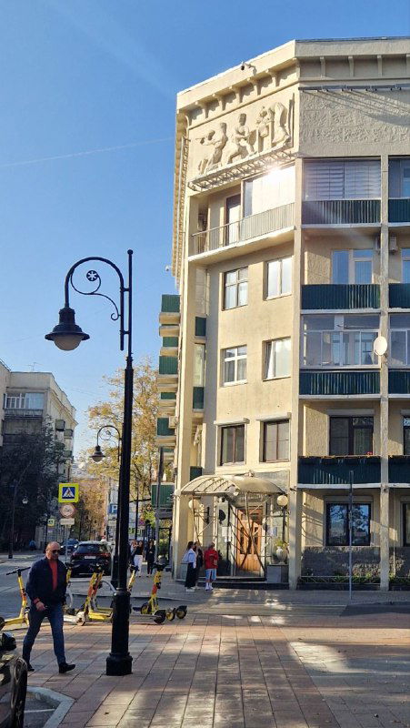 Уличный угол с постконструктивистским зданием и современными элементами: фонари, пешеходы и динамичная городская сцена на Спиридоновке.