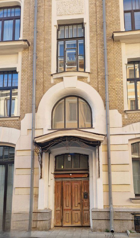Декоративный вход в доходный дом эпохи модерна: массивная деревянная дверь, арочный портал и кирпичная отделка фасада на близком плане.