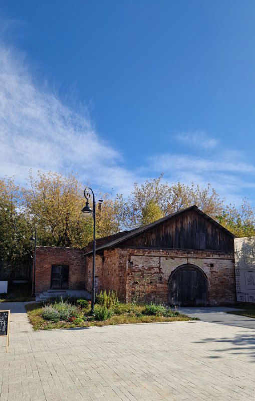 Старинный кирпичный хозяйственный корпус в центре Серпухова: тёплая кирпичная кладка, фонарь и просторно выложенная площадь под небом.