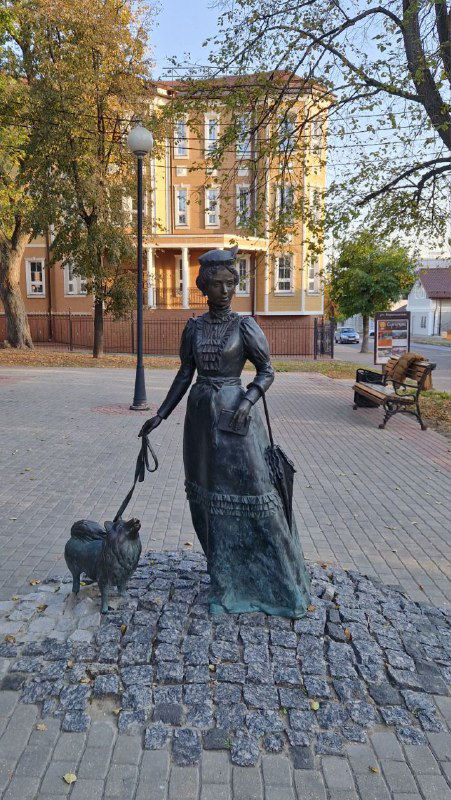 Скульптура женщины с собачкой на поводке на пешеходной площади Серпухова: брусчатка, фонари и лавочки вокруг в осенней обстановке.