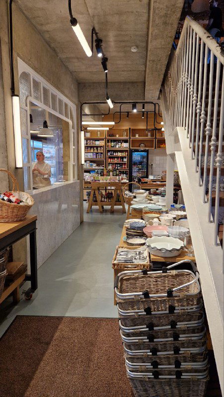 Интерьер местного кафе или магазинчика: аккуратно расставленные корзины и товары, витрина, лестница и уютная атмосфера для остановки на кофе.