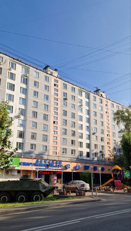 Фасад многоэтажного жилого дома на Профсоюзной улице в Коньково с магазинами на первом этаже и городской улицей на переднем плане.