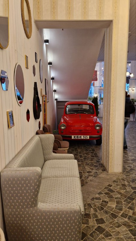 Уютная зона с серым диваном и ярким ретро-автомобилем красного цвета в проходе — фотозона в стиле советских интерьеров и городского эпатажа.