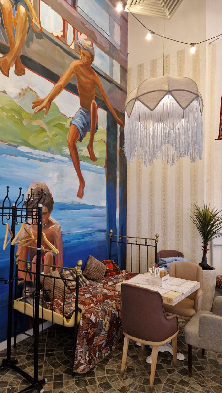 Большая настенная роспись с фигурами людей на фоне, рядом столики и мягкие кресла — сочетание художественных муралов и камерных обеденных зон.