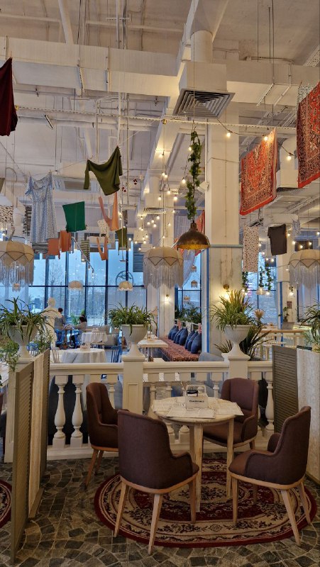 Общий вид зала кафе с высокими окнами, подвешенным бельём как декором и изящными столиками: интерьер в стиле советской эстетики с современным декором.