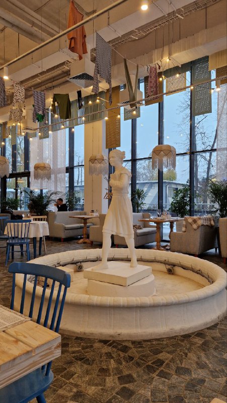 Скульптура в центре небольшого фонтанчика внутри кафе, вокруг столики и высокий потолок — ещё одна декоративная точка для фотографий посетителей.