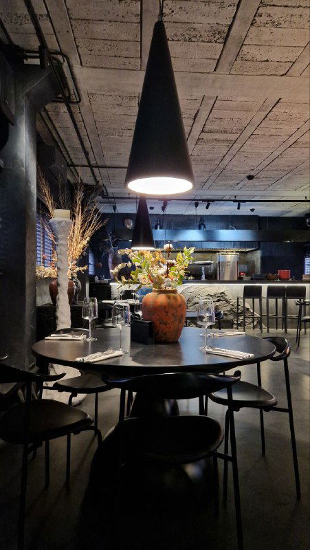 Интерьер ресторана «Коллектив»: тёмная столовая зона с круглым столом, подвесным светильником и декоративной композицией цветов на столе.