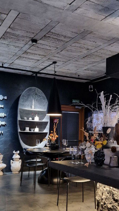 Большая зона ресторана с бетонным потолком, элементами декора в стиле конструктивизма и открытой демонстрацией сервировочной посуды на полках.