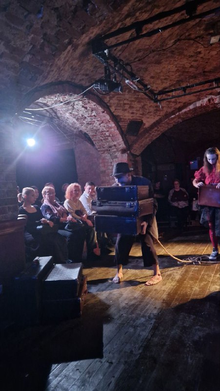 Зрители вблизи сцены: небольшая аудитория, люди внимательно смотрят спектакль в камерном пространстве с низкой аркой и прожекторами.