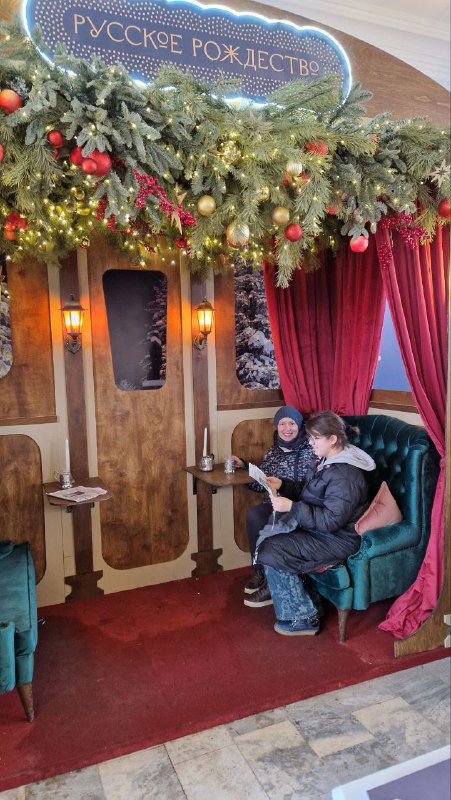 Интерьер вокзала с рождественским оформлением: уютная фотозона фестиваля «Русское Рождество», занавеси и кресла для гостей.