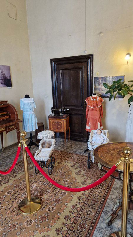 Музейная витрина с детской коляской и старинными игрушками за декоративной оградой в усадьбе М.А. Павлова; экспонаты быта и детства конца XIX — начала XX века.