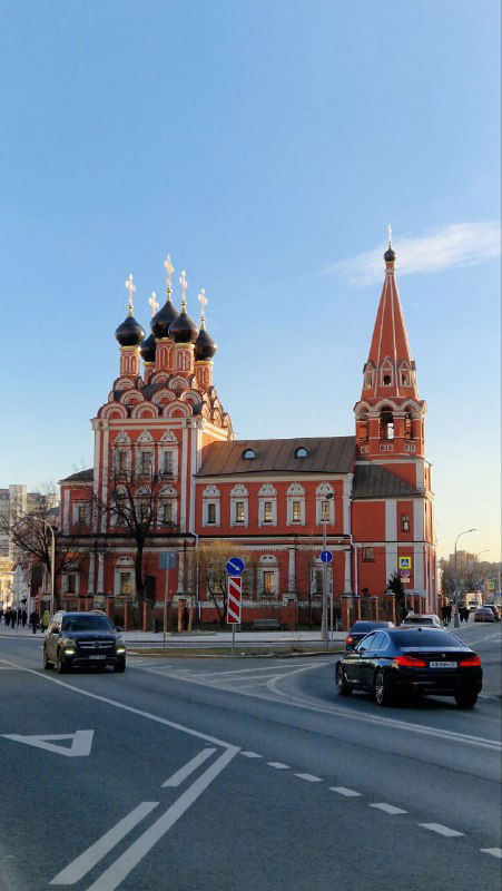 Вид на красочную церковь с куполами и высокой острой колокольней на фоне голубого неба — городской храм вблизи дороги.