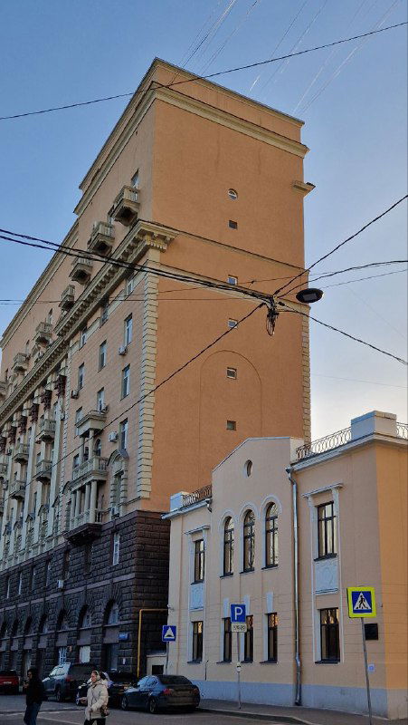 Высокое жилое здание сталинской эпохи с характерными балконами и крупными объёмами, вид с городской улицы и дорожного полотна.