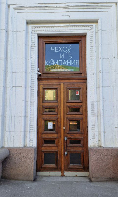 Деревянная входная дверь с оконной вставкой, на стекле надпись «Чехов и компания» — фасад книжного магазина/кофейни.