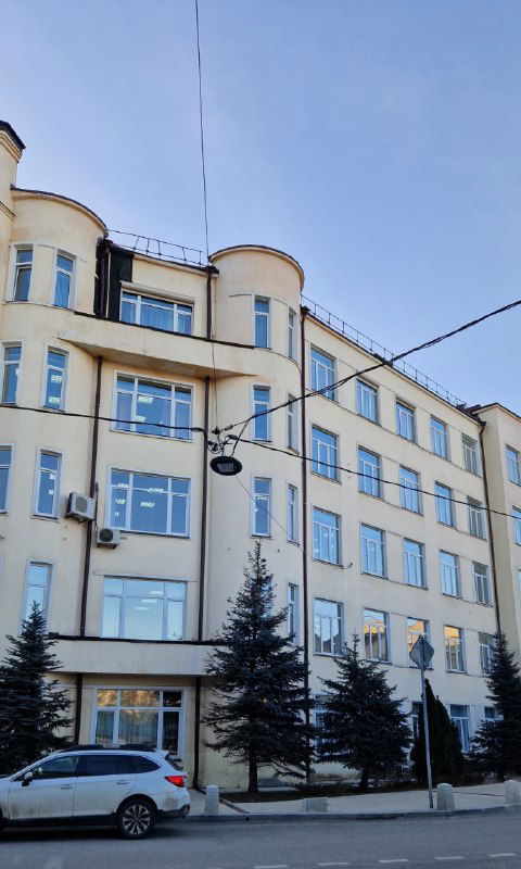 Здание с элементами конструктивизма — строгие геометрические формы, белые стены и крупные прямоугольные окна в городской застройке.