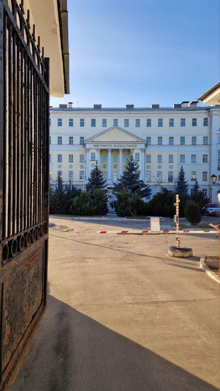 Вид через ворота на внутренний двор и белое административное здание — перспектива входа в институт или крупный комплекс.