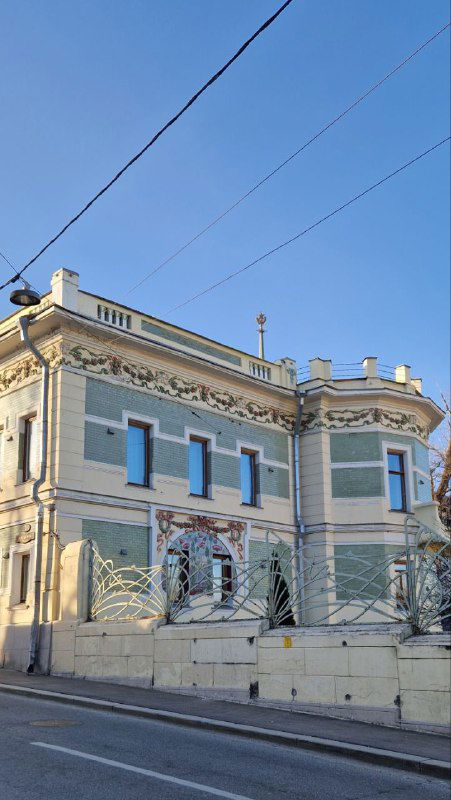 Красивый особняк в стиле модерн на тихой улице: декоративная лепнина, светлая фасадная окраска и архитектурные растительные орнаменты на окнах.