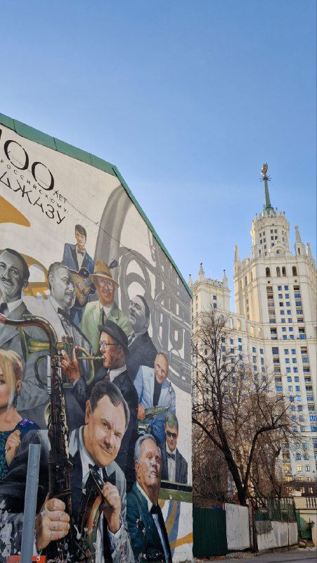 Мурал и фрагменты настенной росписи на фоне высотки на Котельнической набережной: большие лица, сцены и коллажи городских персонажей.