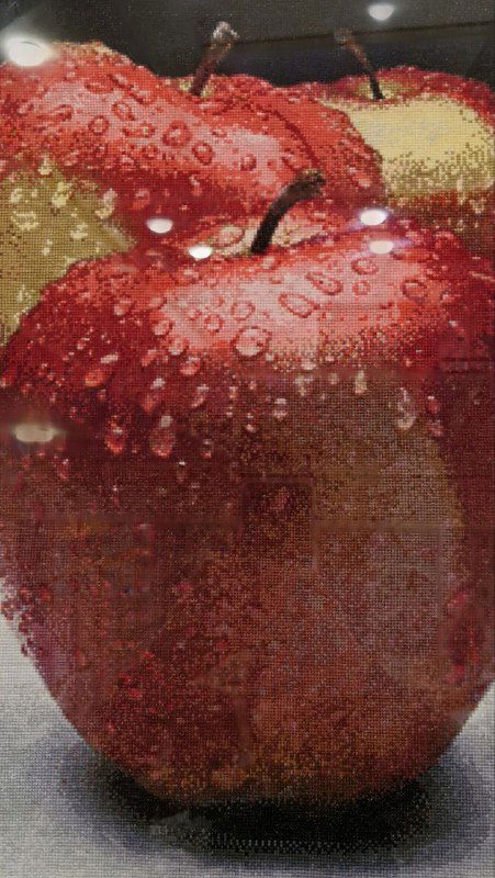 Фрагмент вышитого яблока с каплями росы — деталь экспозиции декоративной вышивки, крупный план текстуры и цвета.