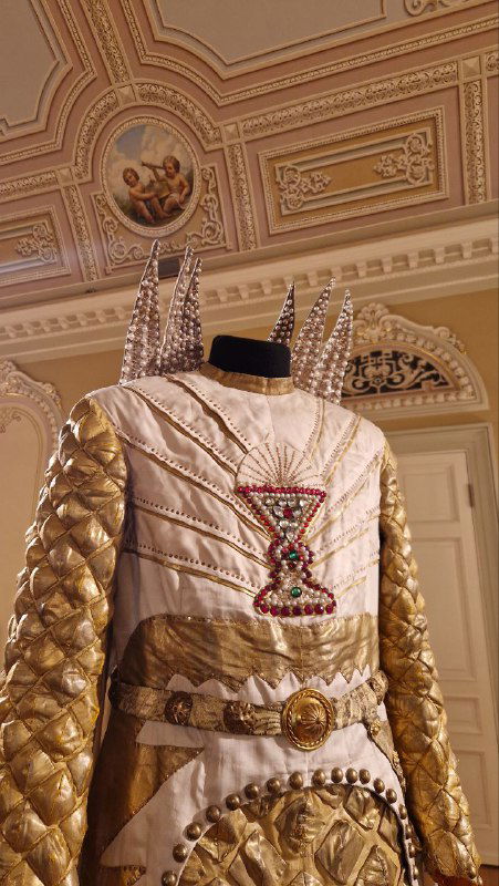 Театральный костюм или реквизит с вышивкой и золотой отделкой, выставленный в фойе или репетиционной зоне — пример сценического убранства.