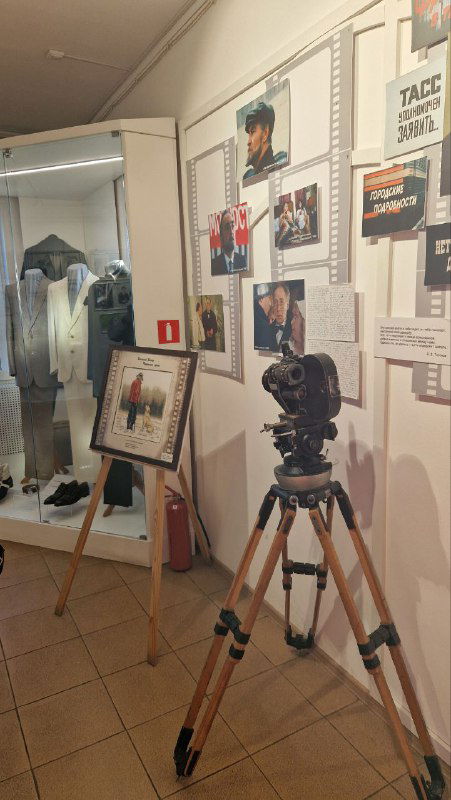 Витрина с кинооборудованием и старой кинокамерой на треноге, экспонаты, иллюстрирующие киносъёмочный процесс и реквизит из фильмов.