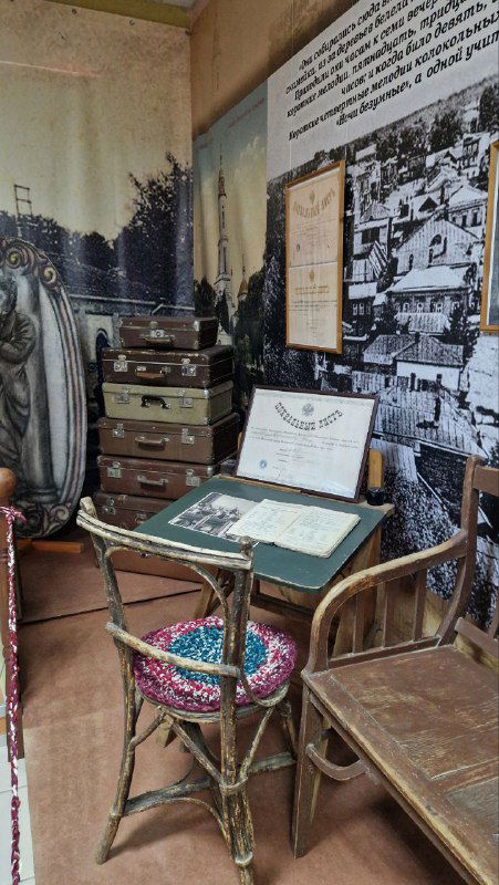 Уголок музейной экспозиции с рабочим столом, чемоданами и стендом с фотографиями и документами, атмосферный интерьер исторического зала.