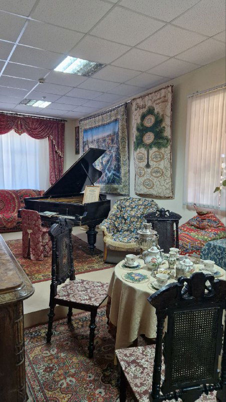 Зал с роялем, диваном и экспонатами текстильного интерьера: ткани, покрывала и сервиз на столике создают атмосферу времени.