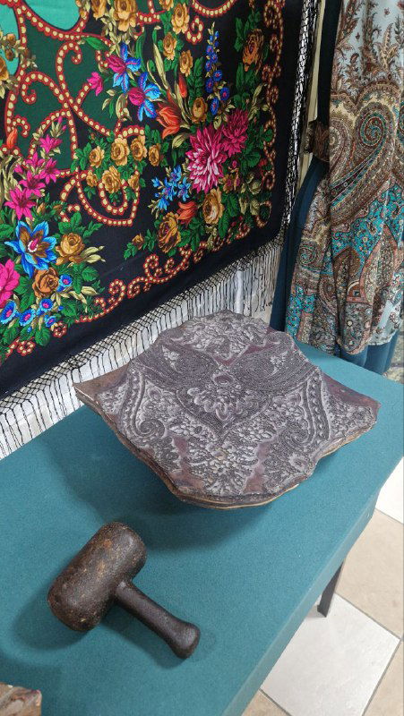 Детальный кадр павлопосадских платков и промышленных инструментов: деревянный молоток и декоративная коробка на столе у экспонатов.