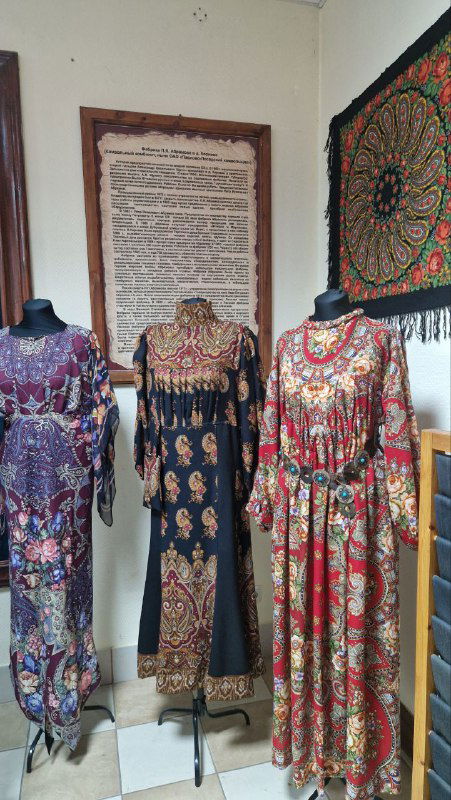 Манекены в традиционных платьях и шали павловопосадского типа, выставленные в витрине, демонстрируют исторические костюмы и орнаменты.