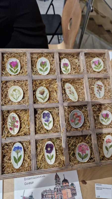 Коробки с керамическими сувенирами крупным планом: декоративные миниатюры с цветочными мотивами и аккуратно уложенными подписи‑ценниками.