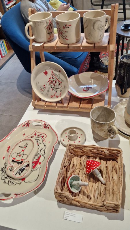 Подставка с керамическими изделиями: тарелки, чашки и небольшие фигурки ручной работы, разложенные для продажи и просмотра.