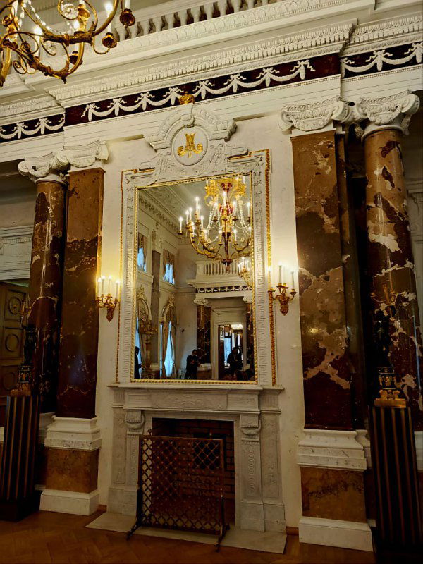 Интерьерный фрагмент с камином, мраморными колоннами и большим зеркалом в золочёной раме — парадная обстановка дворцового зала.