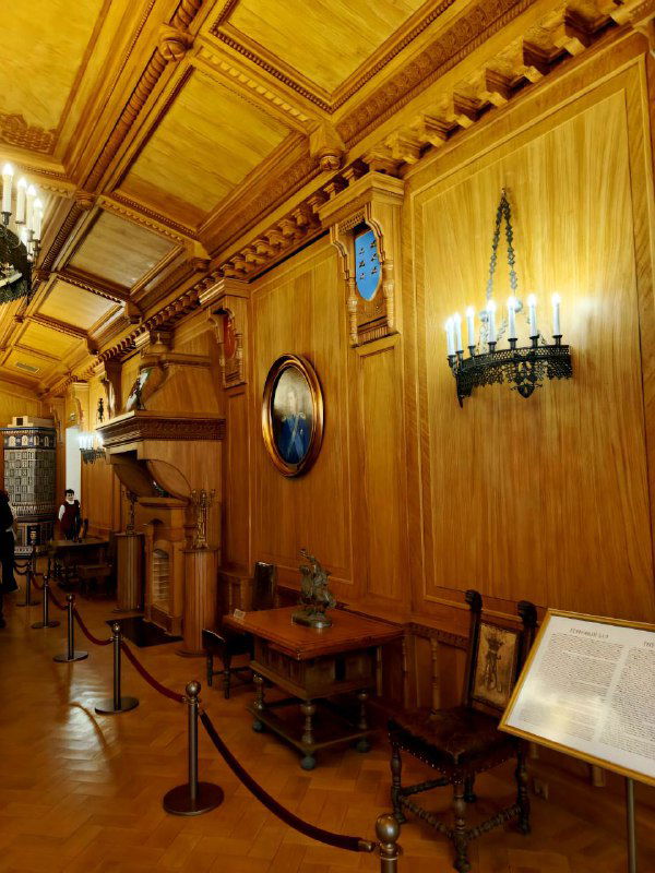 Деревянная панельная отделка коридора дворца: настенные часы, бра и небольшие картины в овальных рамах создают камерную атмосферу.