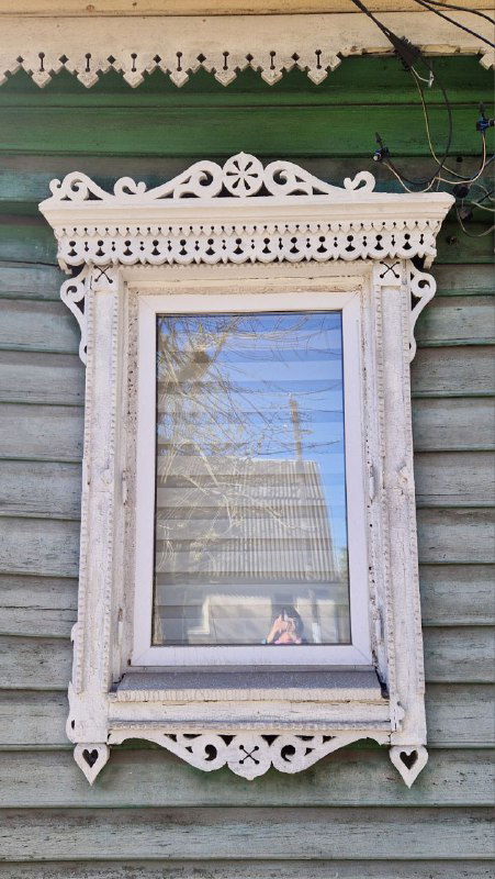 Белый резной наличник вокруг окна на деревянном доме, тонкая ажурная резьба характерна для наличников конца XVIII — XIX века в Твери.