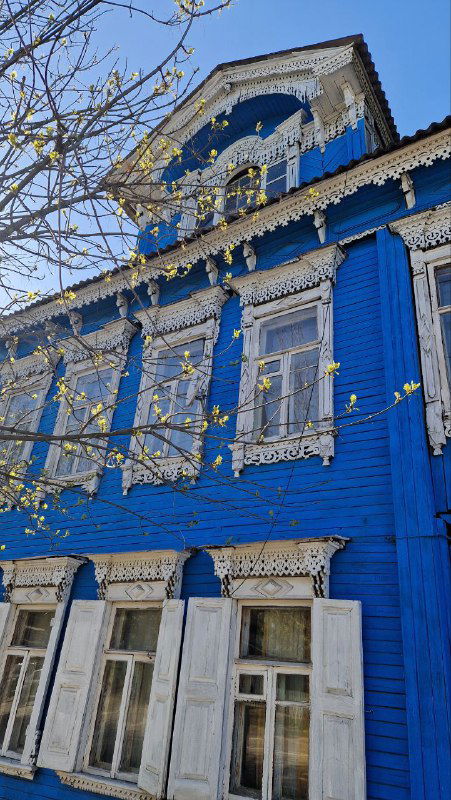 Синий двухэтажный деревянный дом с колонными и резными наличниками — общий вид фасада и окон в историческом районе Затьмачья в Твери.