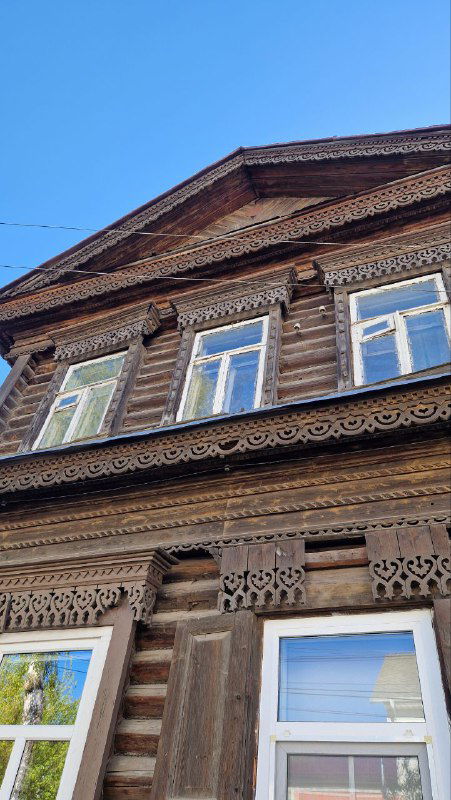 Коричневый деревянный фасад с рядами резных наличников над окнами и геометрическим орнаментом, общий вид фасада дома в историческом районе.