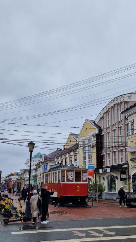 Пешеходная улица с ретро-трамваем в Твери, витрины кафе и прохожие под плотным серым небом в историческом центре города