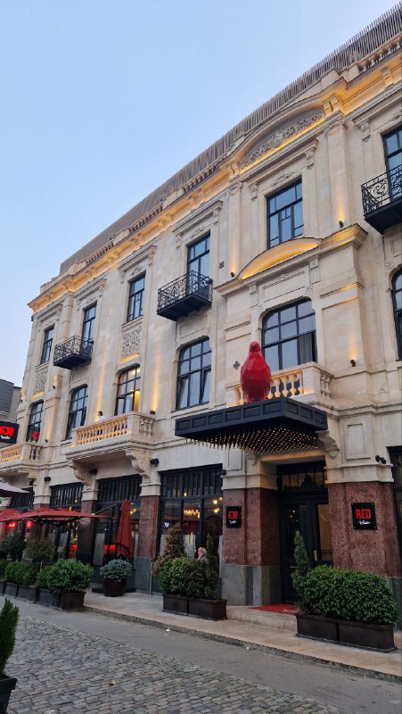 Фасад здания с декором и уличными кафе на большой архитектурной улице Тбилиси, вечернее освещение и пешеходная зона.