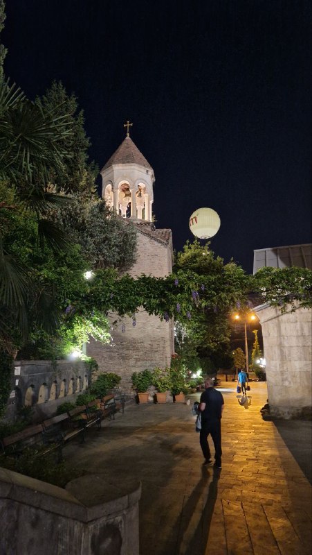 Подсвеченный Сионский собор ночью, а рядом большая рекламная луна на здании — городской панорамный вид с неоновым акцентом.