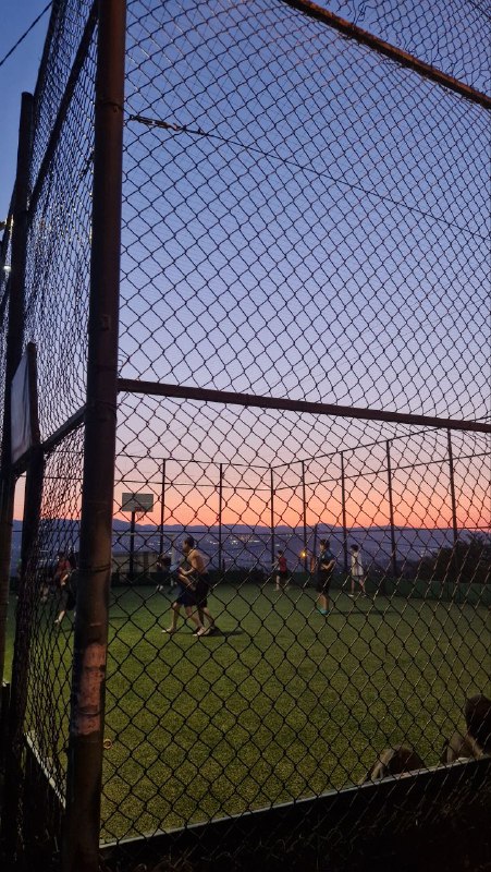 Футбольное поле у ограждения на закате: игроки и розовое небо вдалеке — найденная смотровая площадка с видом на город.