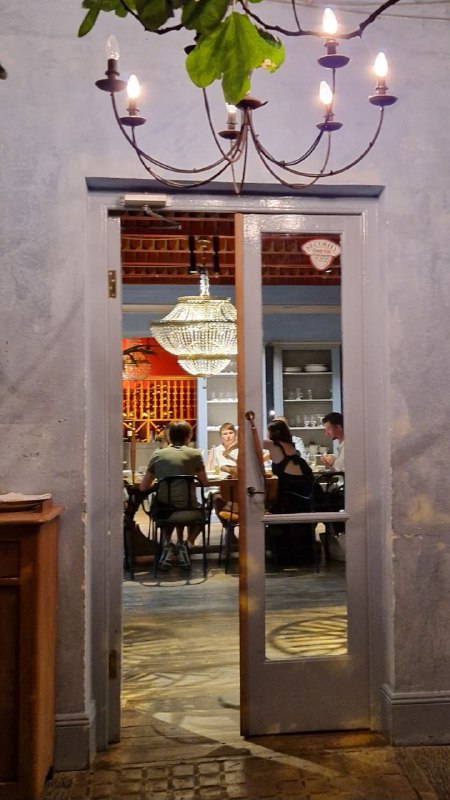 Двери и люстра, вид через проём в зал ресторана: гости за столами, крупная люстра и уютный интерьер в стиле старой тбилисской квартиры.