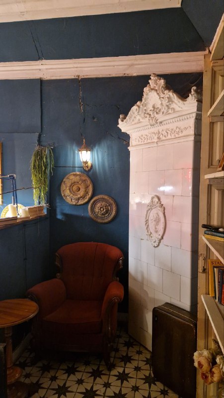 Уютный уголок с высокотопочной печью, креслом и декоративными тарелками на стене — ощущение домашнего интерьера внутри кафе-ресторана.