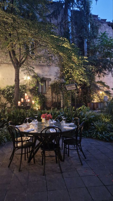 Стол сервированный на открытой площадке среди зелёных насаждений: тарелки и свечи создают романтичную атмосферу в дворе ресторана.