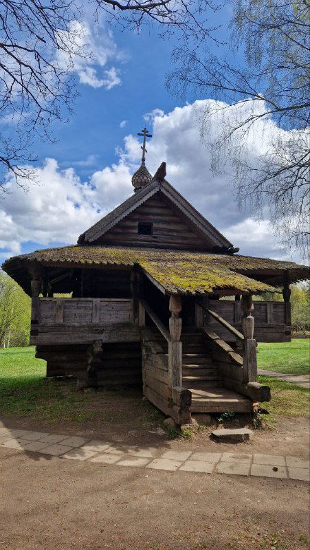 Старинное деревянное строение с крыльцом и моховой кровлей, видны ступени у входа и характерная резная отделка фасада усадебного дома.