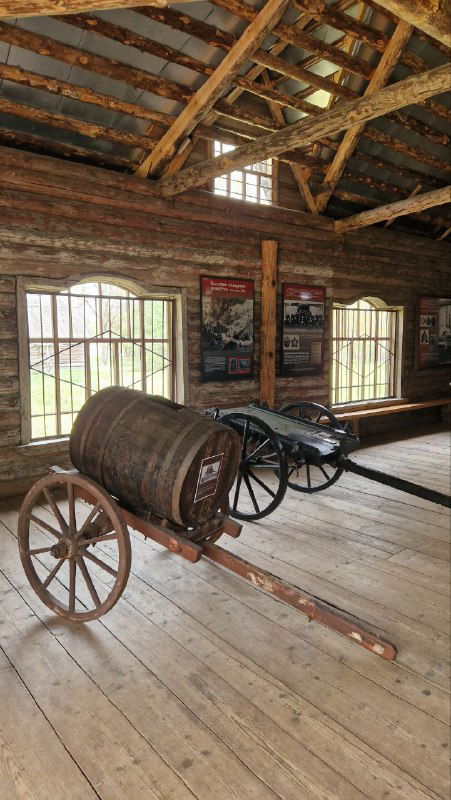 Интерьер амбара: массивные деревянные балки, старинная телега и предметы быта — тематическая экспозиция XVIII–XIX веков в музее.