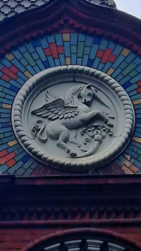 Крупный декоративный медальон на фасаде с изображением крылатого единорога на фоне цветных изразцов — один из загадочных орнаментов терема.