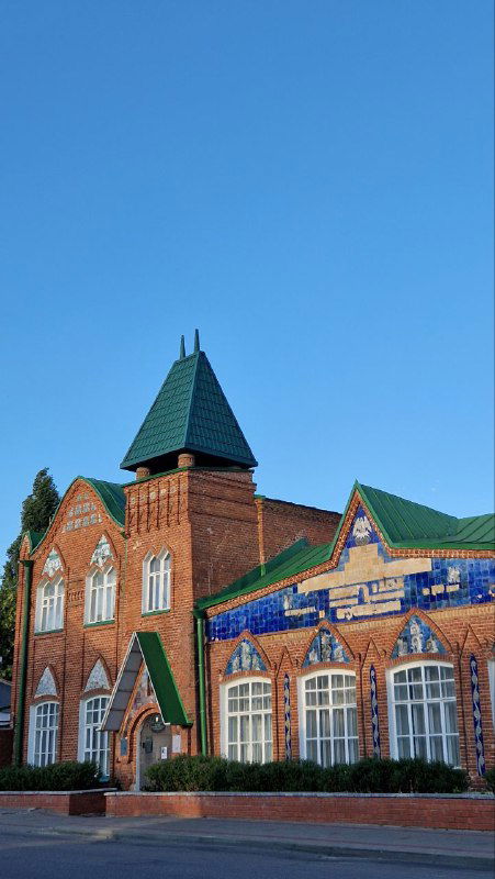 Яркое кирпичное здание с зелёной крышей и декоративными керамическими вставками, архитектурный акцент в городской застройке Ельца.