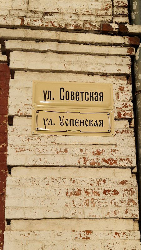 Старинная фасадная табличка с дореволюционными названиями улиц на кирпичной стене; городская навигация и историческая стилистика.